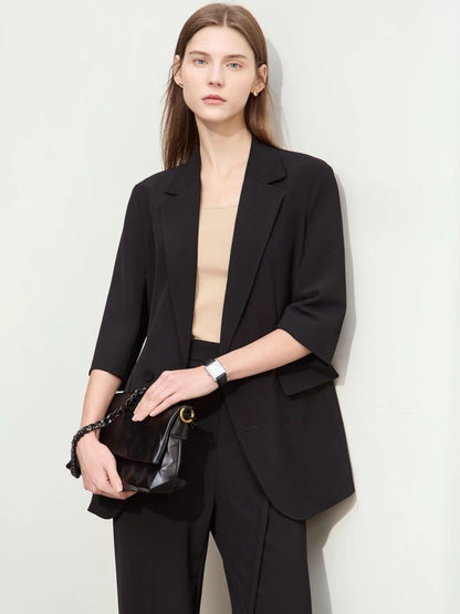 Schwarzer Hosenanzug mit 3/4-Arm-Blazer, Modell frontal mit Clutch.