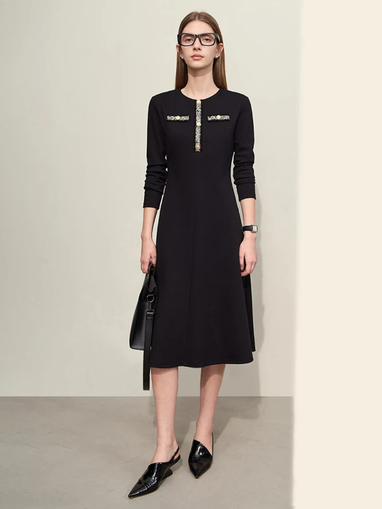 An elegant woman wearing a military inspired dress. The dress has long, fitted sleeves and an a-line silhouette. The bodice showcases a gold embroidery design with buttons. 