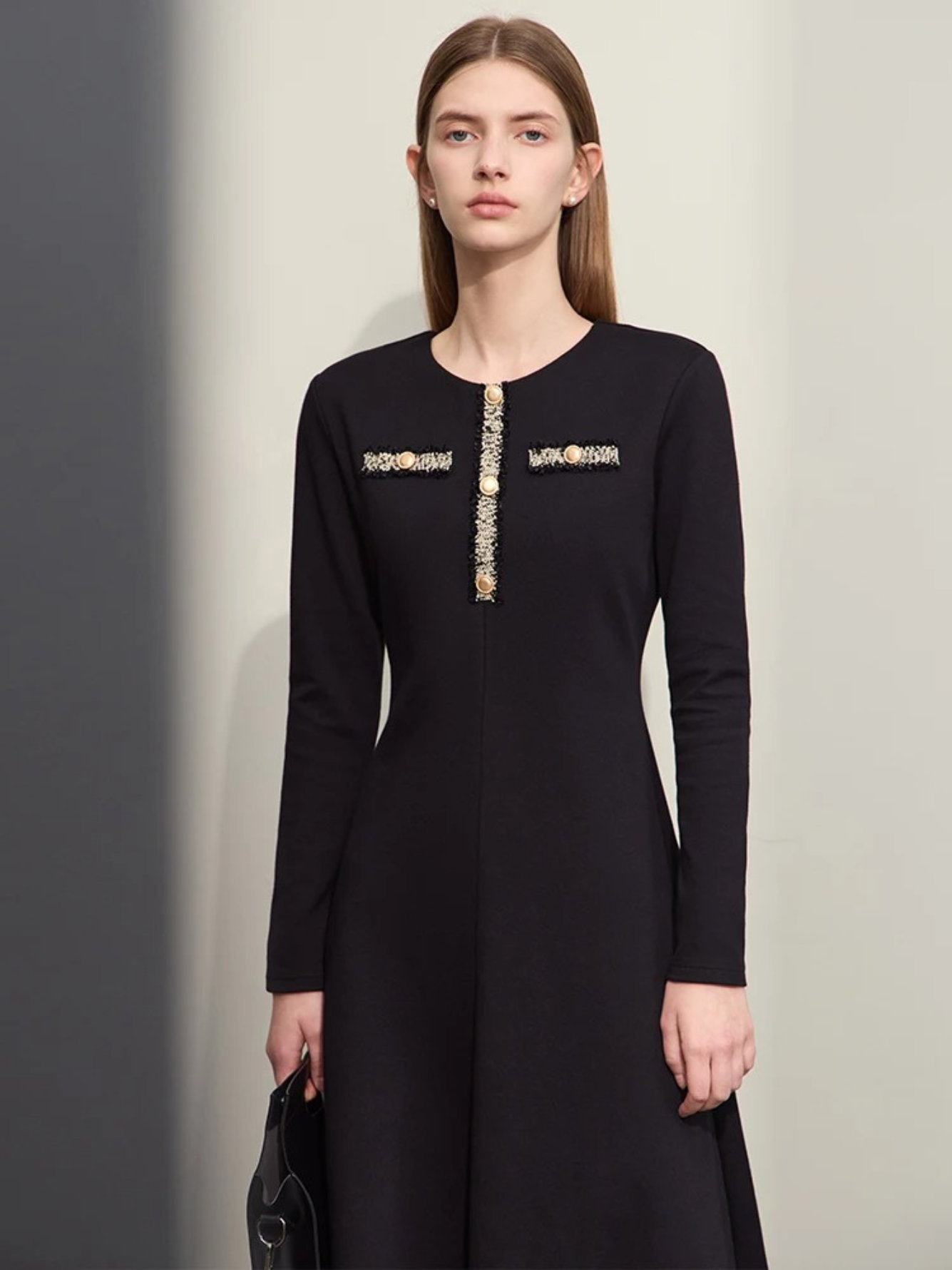 An elegant woman wearing a military inspired dress. The dress has long, fitted sleeves and an a-line silhouette. The bodice showcases a gold embroidery design with buttons. 
