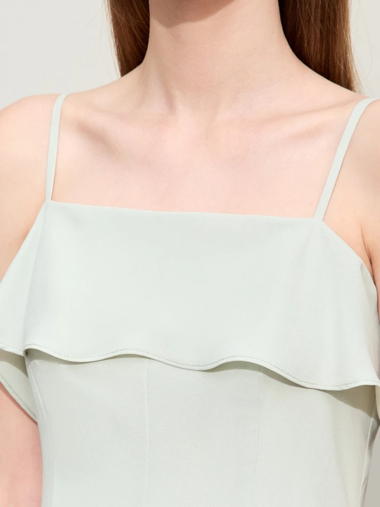 Close up of the bodice of a minimalist and simple dress in mint green featuring thin straps and a ruffle design.