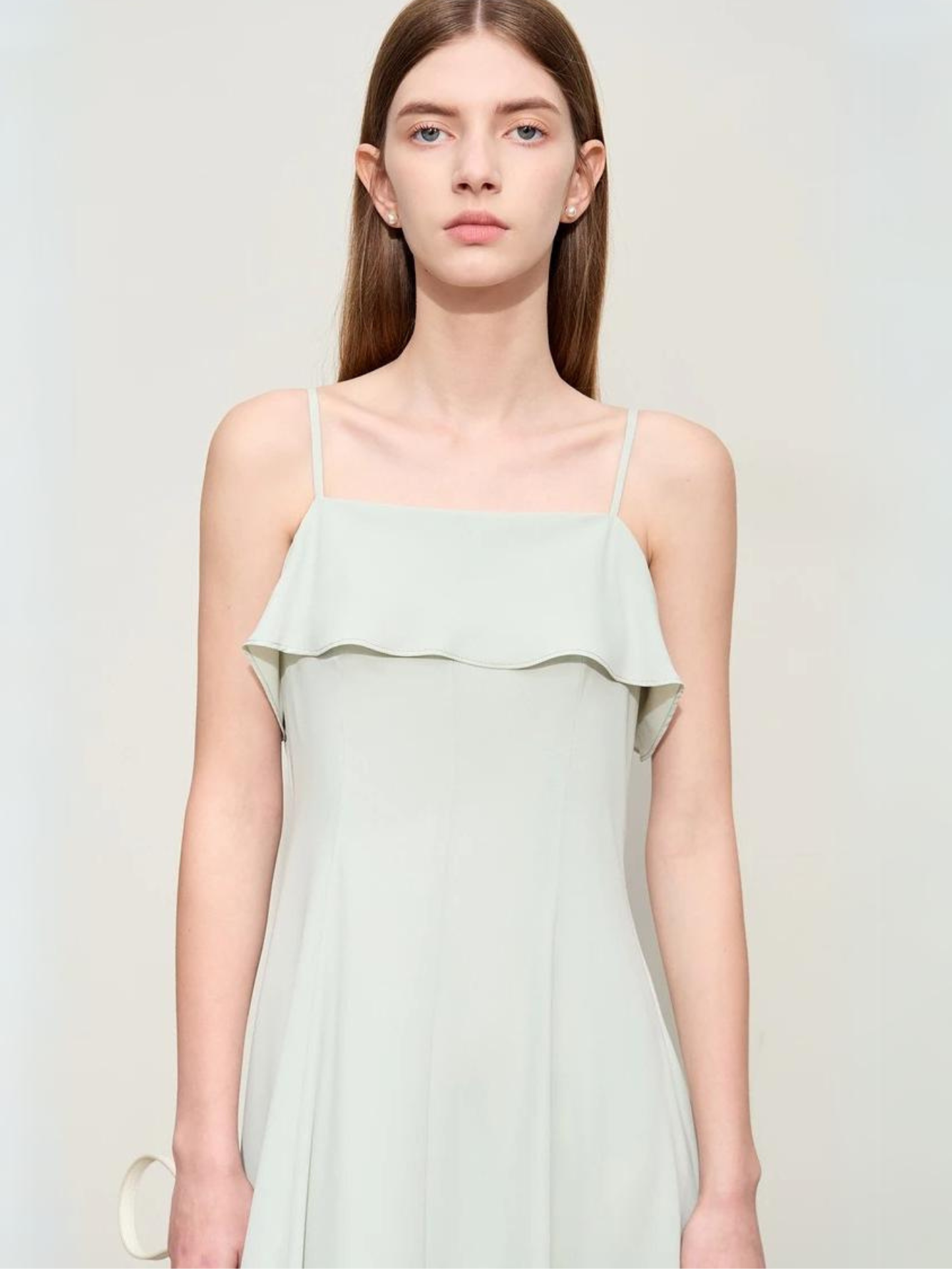 A brunette woman wearing a simple and minimalist chiffon dress in mint green.