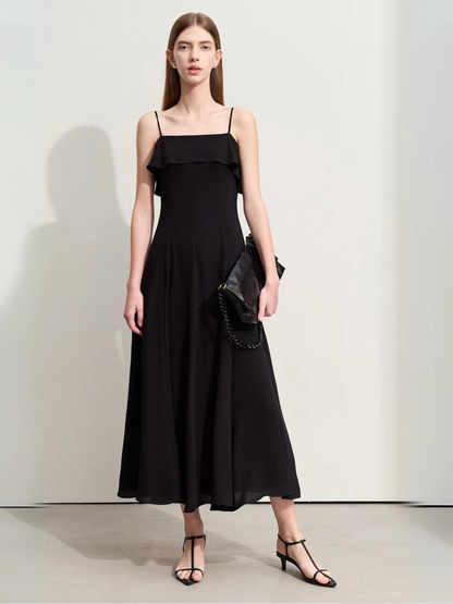 A woman wearing a black, simple, angkle-length dress in black with strappy kitten hills holding a black purse.