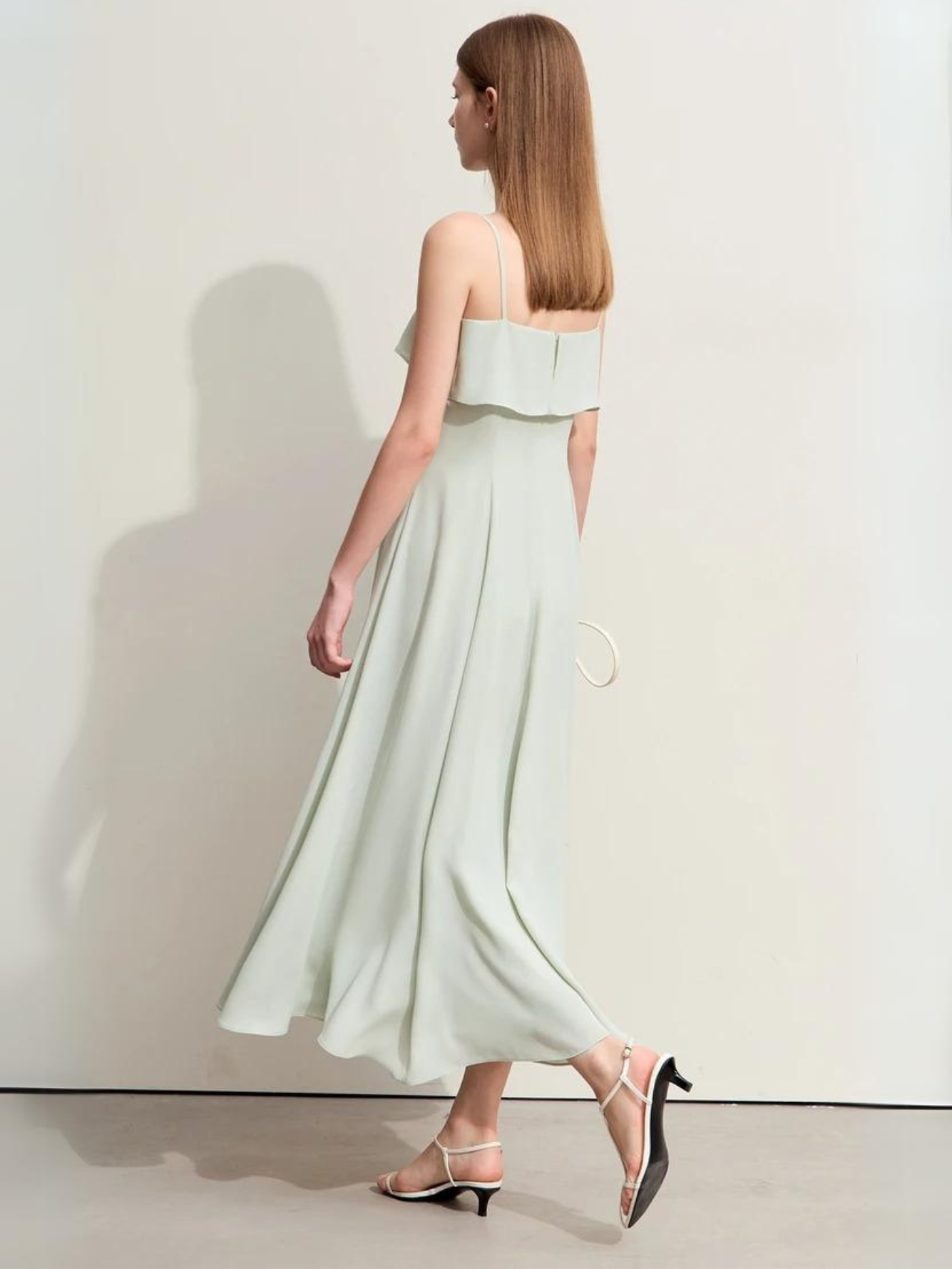 A woman walking away wearing a mint green, minimalist chiffon ankle-length dress with white strappy kitten heels.