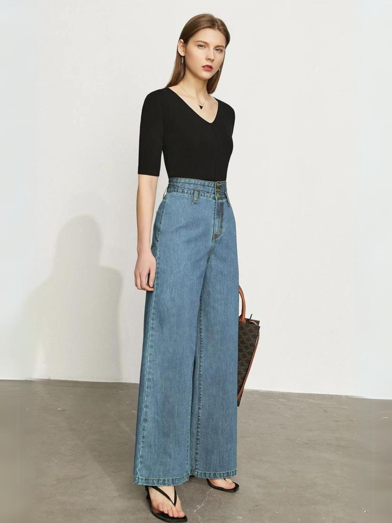 A woman wearing a fitted black shirt with a pair of retro-inspired, wide leg jeans with a cinched waist design and a pair of sandals.