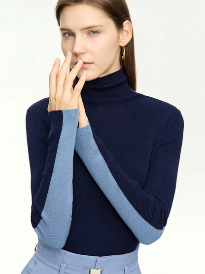 A woman wearing a mock neck, dual toned sweater in light and dark blue with a pair of light blue belted high waisted pants with a belt detail.