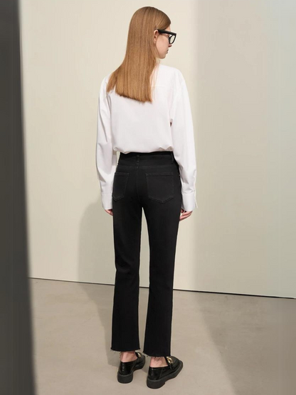 A woman wearing a classic white long sleeve shirt with a pair of black, pencil cut jeans and a pair of loafers.