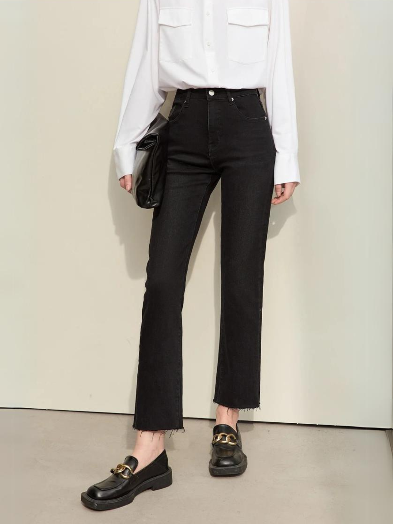 A woman wearing a classic white long sleeve shirt with a pair of black, pencil cut jeans and a pair of loafers.