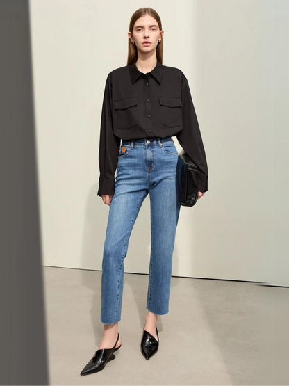 A woman wearing a classic black long sleeve shirt with a pair of denim blue, pencil cut jeans and a pair of pointed heels.